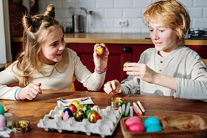 Deti sediace za kuchynským stolom zdobia veľkonočné vajíčka